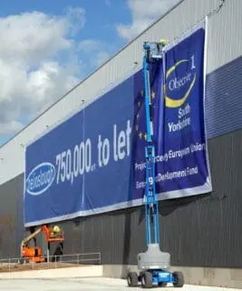 Very large banner printed and displayed on the side of a warehouse building advertising space to let